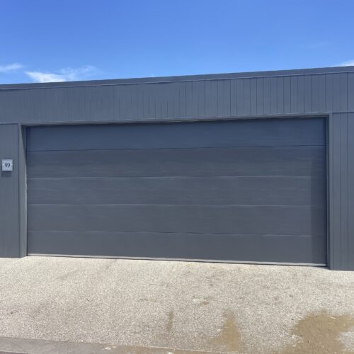 Grey sectional garage door set into a grey clad garage wall