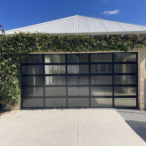Black framed glass panel garage door on a double garage with a pitched metal roof