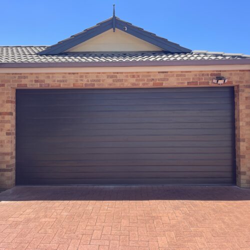 Dark brown sectional garage door on a brick home with a paved driveway