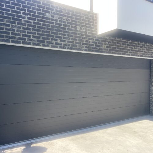Charcoal horizontal panel garage door beneath a dark brick wall