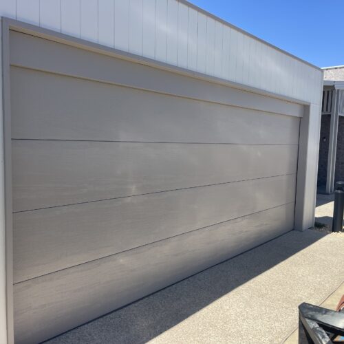 Wide woodgrain-look garage door on a modern home with a white clad frame