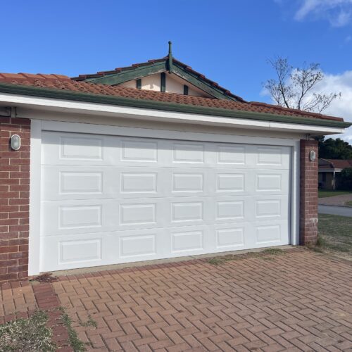 White raised panel garage door on a double garage with a brick facade and paved driveway