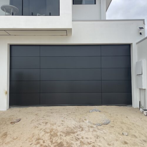 Charcoal panelled garage door on a modern white home with a sandy front yard