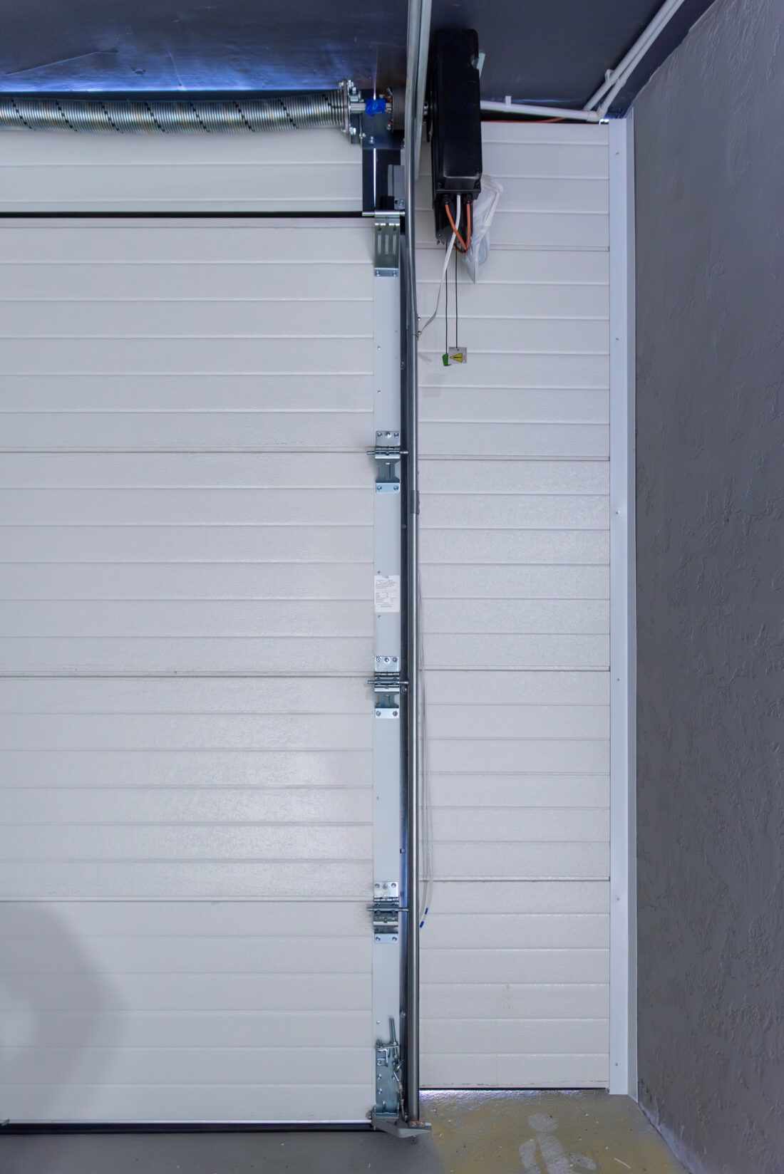 Automatic electric opener on white sectional garage door mechanism